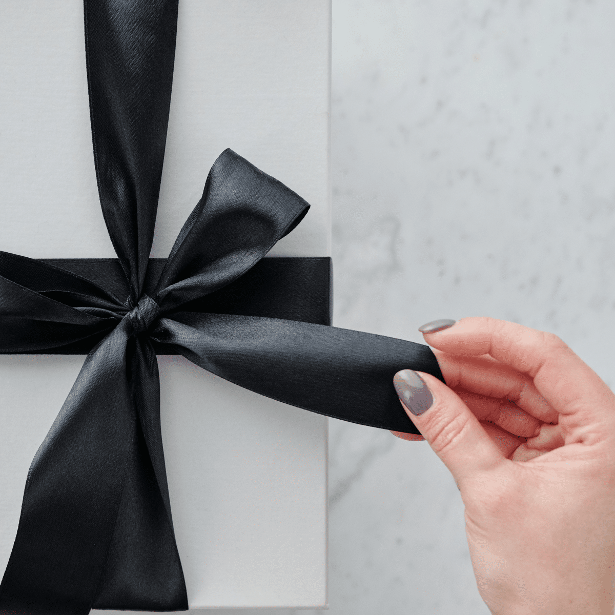 Main dénouant le ruban noir d'un coffret cadeau élégant
